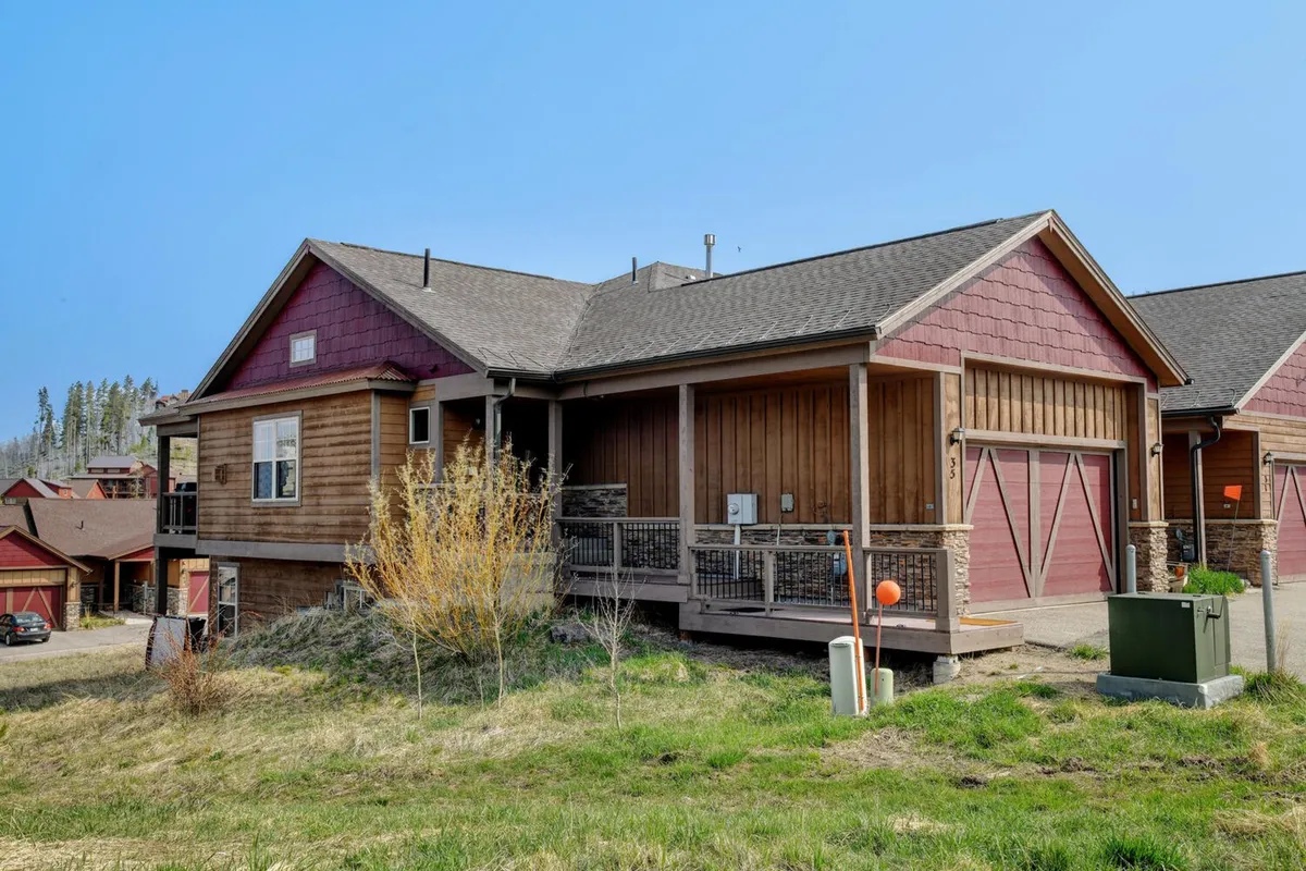 A charming chalet exterior featuring a warm wooden facade with stone accents and a welcoming porch area. The space is surrounded by greenery, offering an inviting environment for outdoor relaxation and socializing, making it ideal for guests and their pets to enjoy mountain air together.