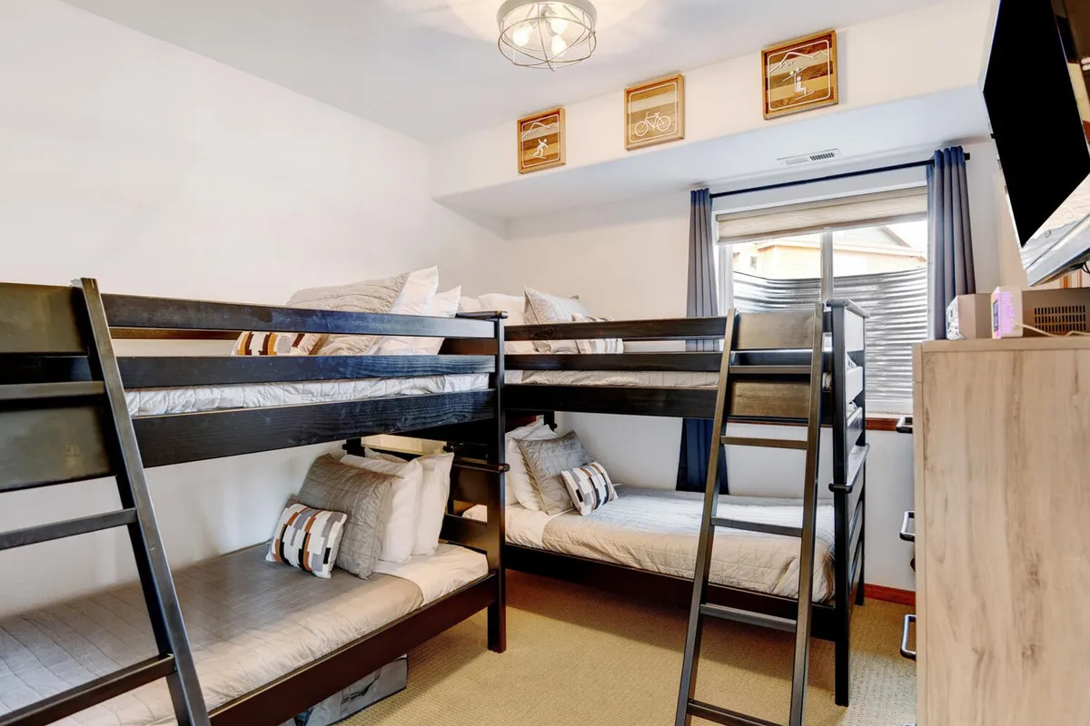 A cheerful bunk room featuring twin bunk beds, colorful wall art, and a storage unit beneath the window. The playful design and functional layout create an ideal space for children or groups to enjoy shared bedtime fun.