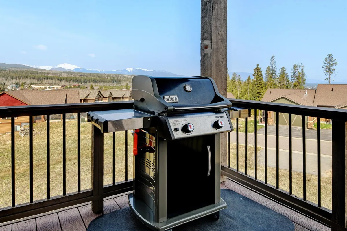 A scenic deck with a grill overlooking stunning mountain views, complemented by a sturdy railing that ensures safety for all family members, including pets. The deck is set up for outdoor dining and socializing, with ample space to lounge and soak in the natural surroundings.