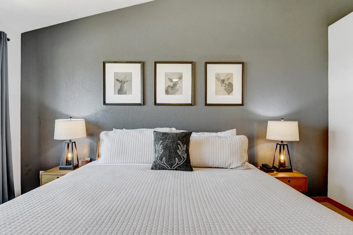 A warmly lit bedroom with a comfortable bed adorned with decorative pillows and a pair of lamps on the nightstands. Framed wall art adds a stylish touch, and the overall atmosphere is serene and welcoming, perfectly suited for relaxation after a busy day.
