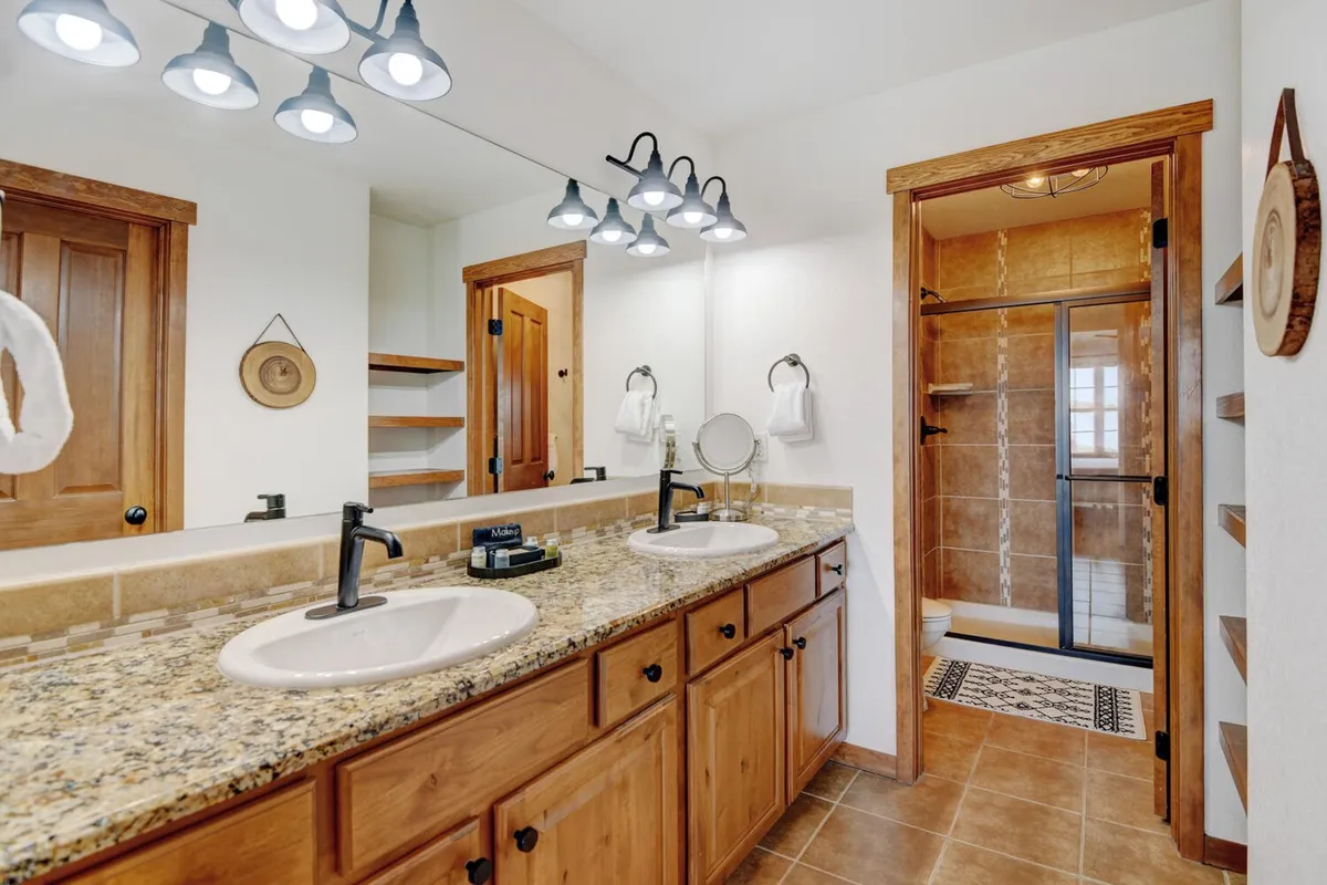A modern bathroom with double sinks set in a granite countertop, a large mirror, and a glass-enclosed shower. The space is immaculately organized, evoking a spa-like feel that encourages relaxation and self-care.