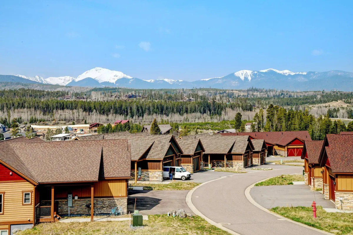 A sweeping view of a mountain range with residential cabins nestled along a curved road. The scene exudes tranquility, inviting guests to envision their stay in a serene alpine setting ideal for outdoor adventures and wellness retreats. The sunrise lighting enhances the feeling of rejuvenation and possibility.