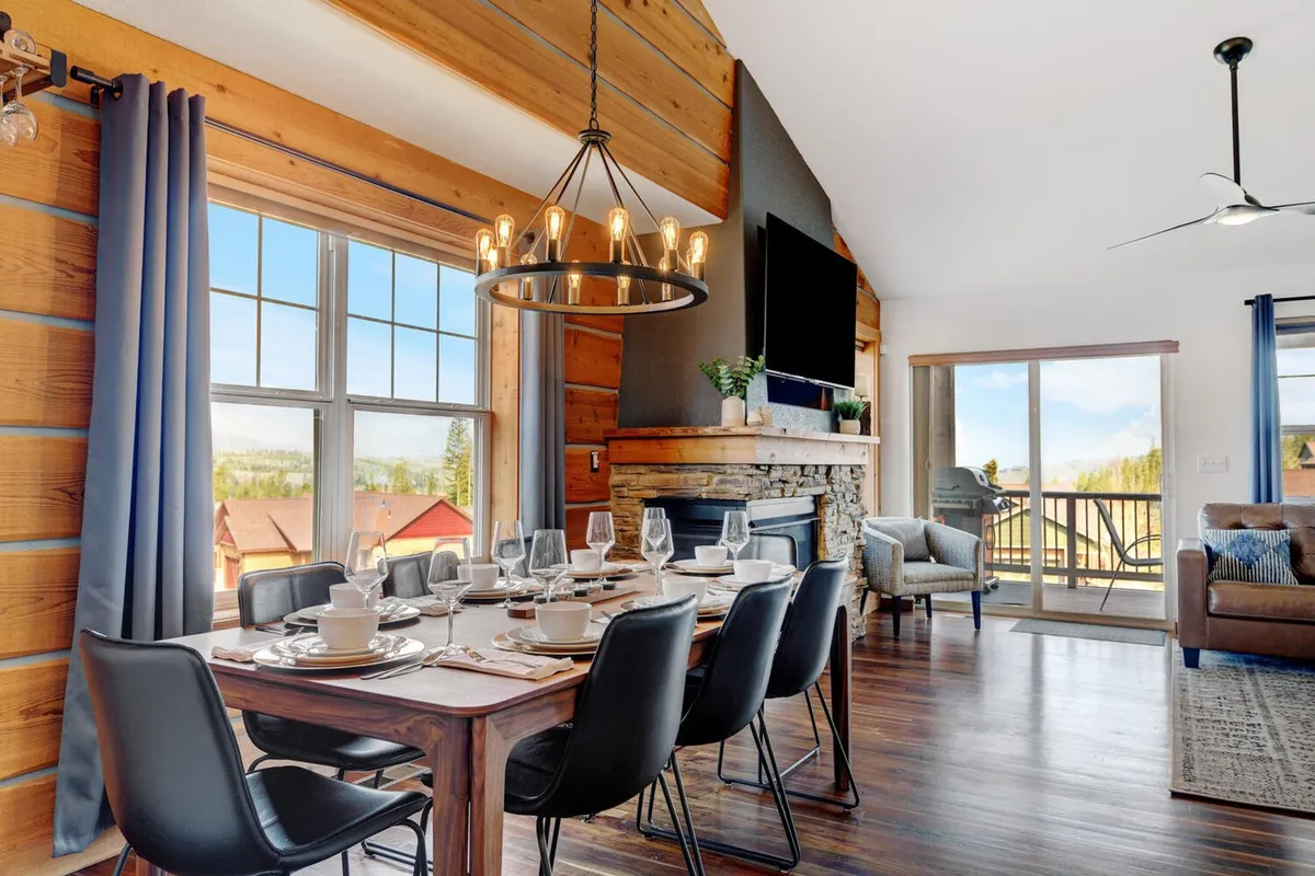 A warm, cozy interior shot highlights the family dining table, a glowing fireplace, and large windows framing scenic outdoor views. The setup is ideal for family dinners, game nights, or relaxing together indoors, inviting families to create lasting memories inside the home.
