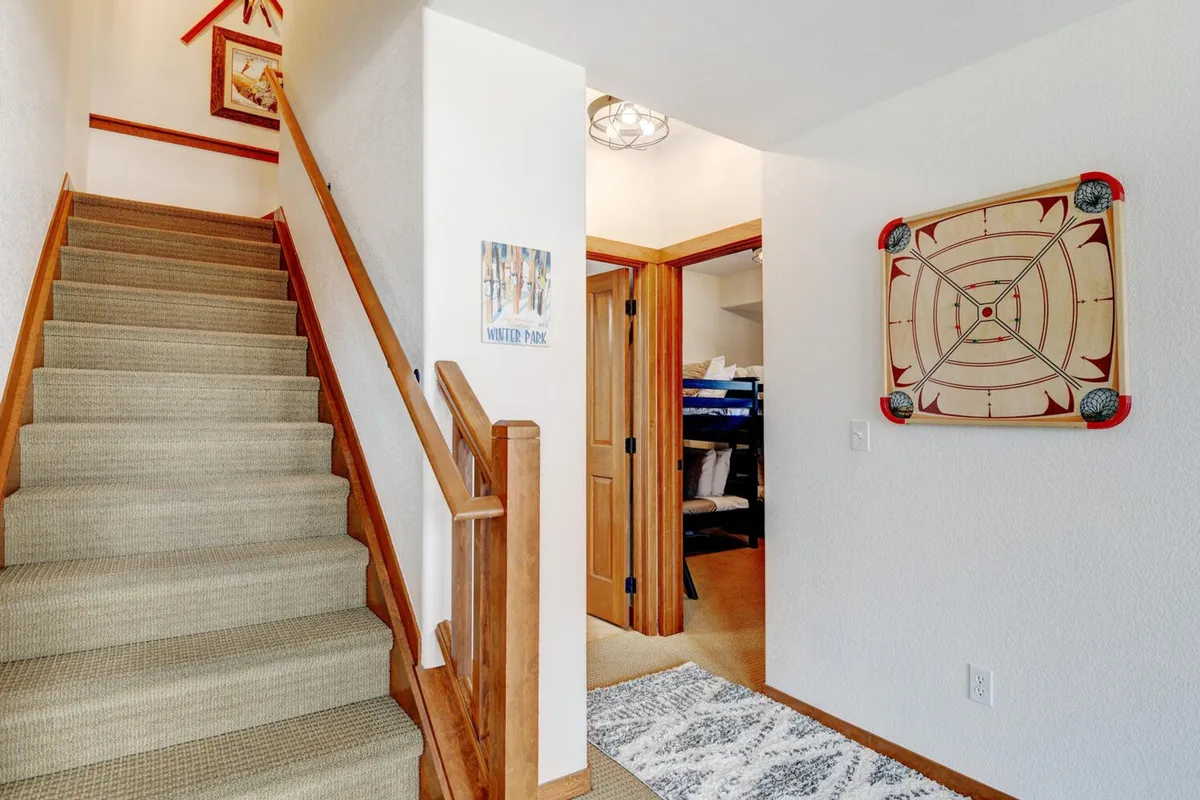 An inviting interior view that includes a staircase with artwork on the wall and a crokinole board, hinting at family-friendly game nights and casual gatherings. The setting is relaxed and encourages playful interaction.